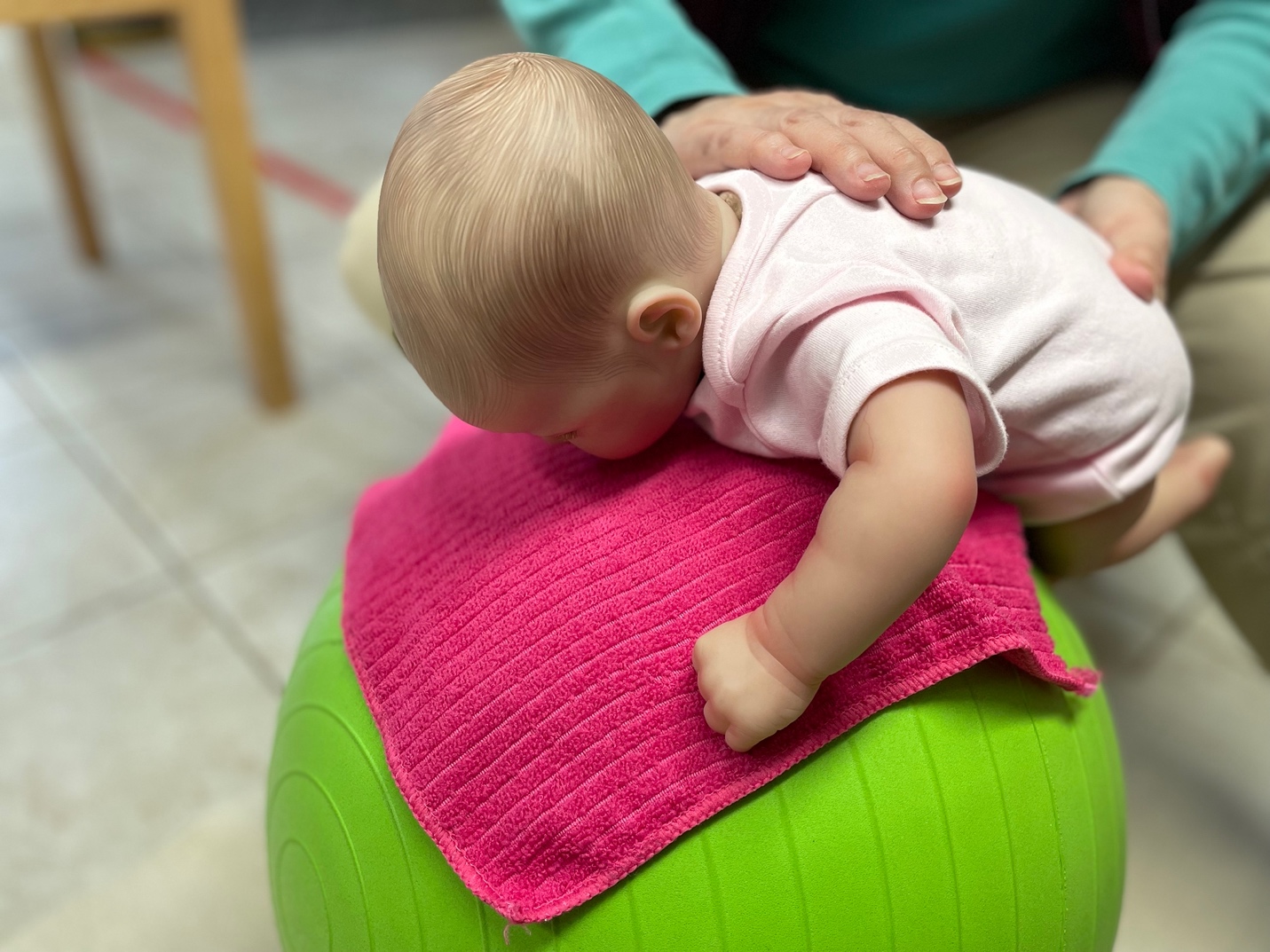 Baby doing tummy time on an exercise ball with caregiver support